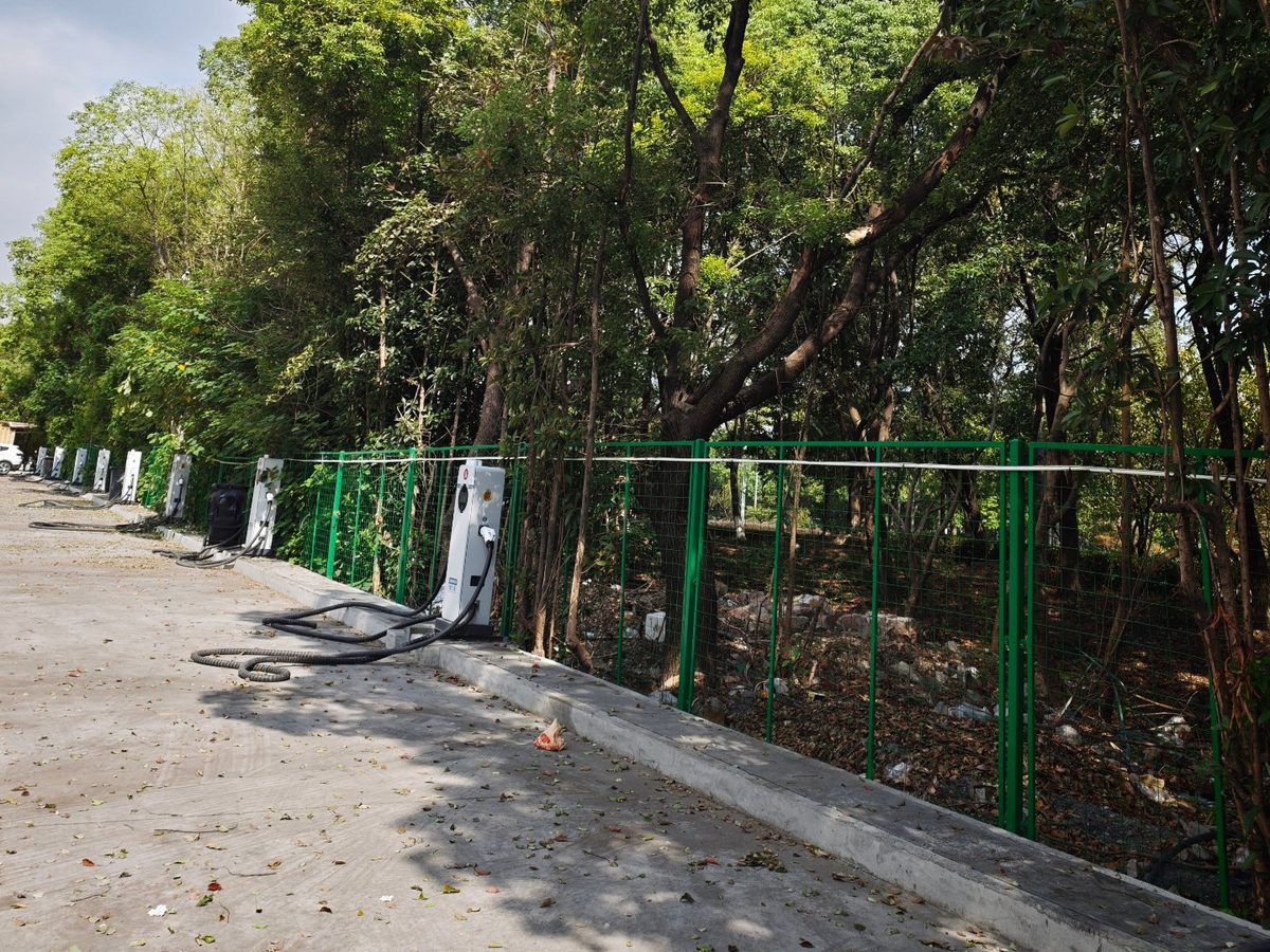 祥荣再生资源场区充电站实拍：绿网围栏与林带一侧成排布置的充电桩位与场地通道