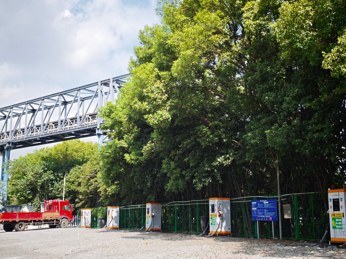 祥荣再生资源场区充电站实拍：桁架桥下一排充电桩，红色卡车与场区运输通道